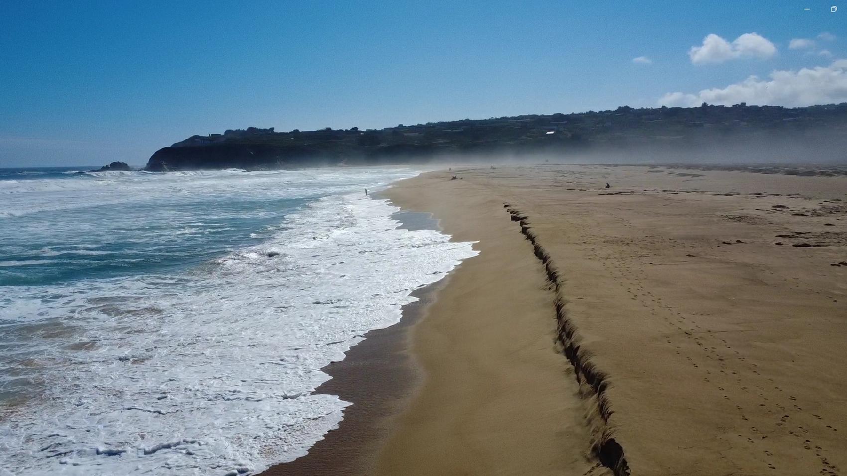 Playa abierta con oleaje y campo dunar vistos desde el aire